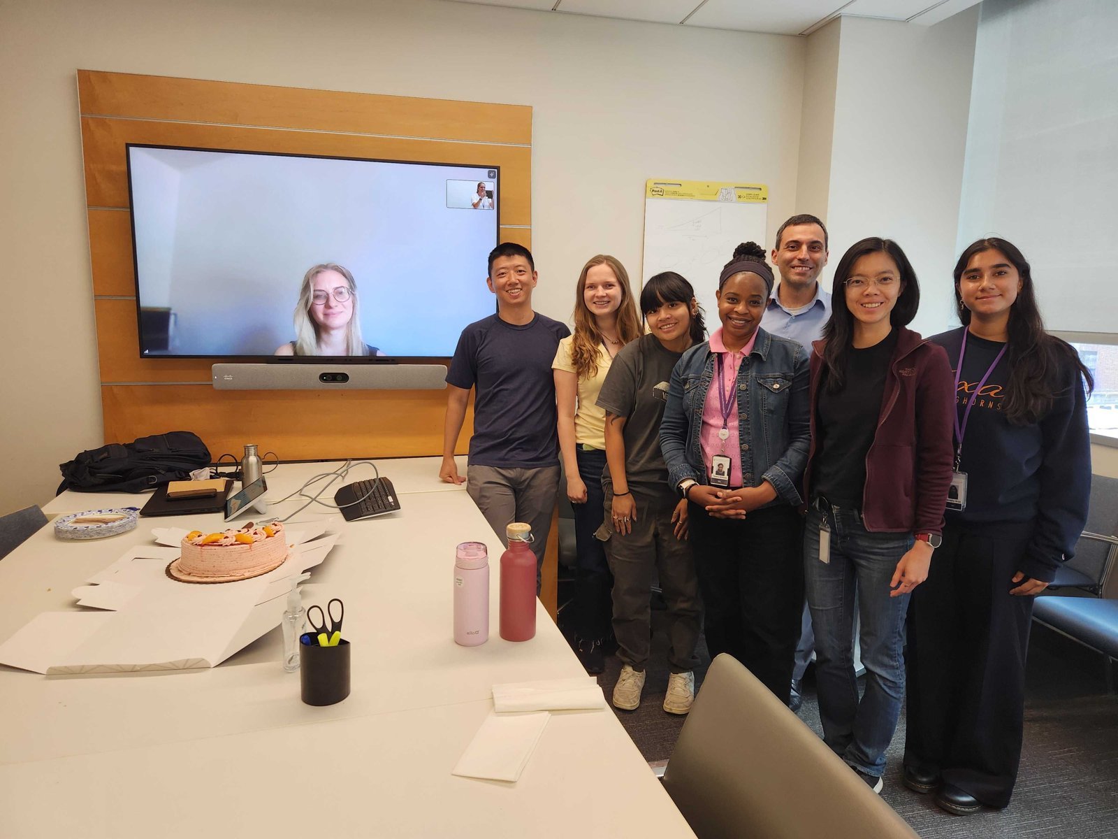 Lab members celebrating with cake, with a colleague joining by video